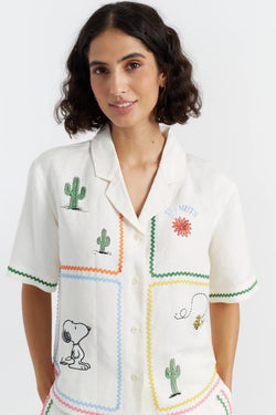 Woman wearing a white blouse with embroidered designs on a plain background