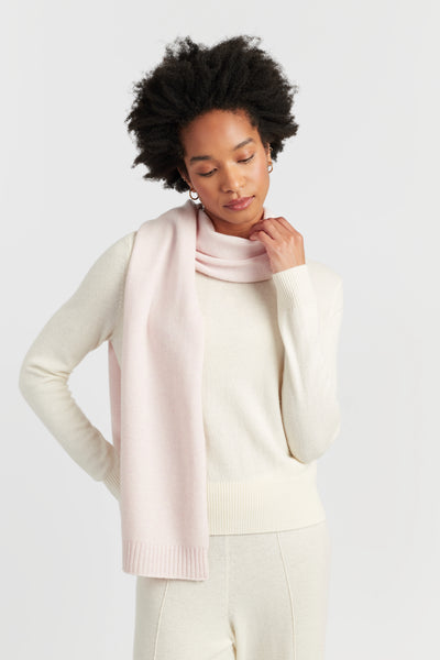 Woman wearing a light pink scarf and white sweater on a plain background