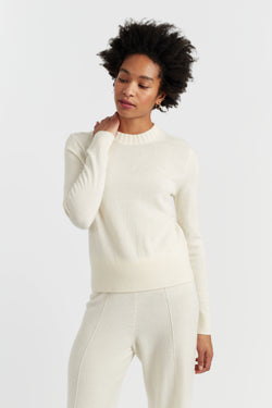 Woman wearing a white sweater and pants on a light gray background