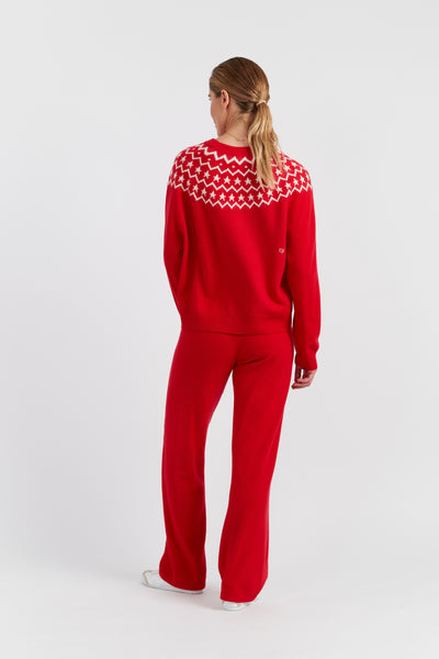 Person wearing a red sweater with a patterned design on the back, standing against a white background