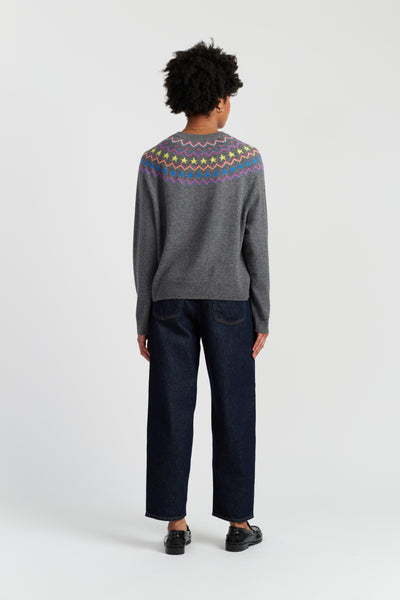 Person wearing a gray sweater with colorful patterns on the back, standing against a white background